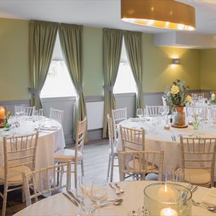 Dining room set out with round tables with white tablecloths, white chairs and table settings