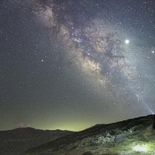 Silhouette of a person photographing The Milky Way from the hillside