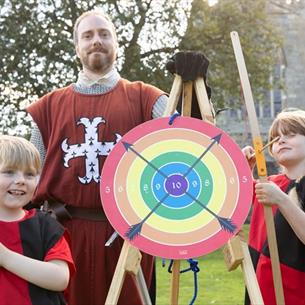An archery target with two children holding bow and arrows with the instructor