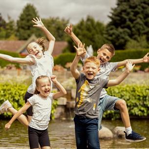 Four children laughing and jumping in the air in front of a pond at Durham University Botanic Garden. 