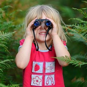 Small child looking through binoculars, surrounded by ferns