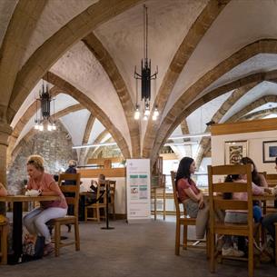 Two families sit at tables in a cafe, which has an arched stone roof.