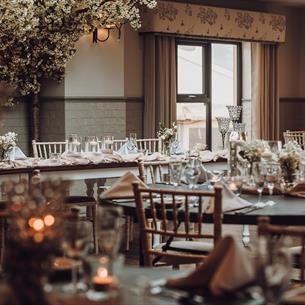 The Orangery, with friendly folk pelmets, soft grey ticking curtains, lime-washed furniture, and clothed tables with floral centrepieces and candles.