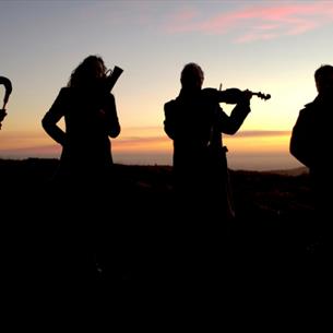 Four musicians silhouetted against a winter sunrise, holding various early musical instruments