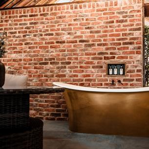 High ceilings, wood panelling, bespoke candle chandeliers and a large free-standing bath against the exposed brick wall.