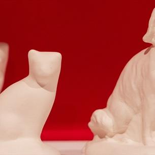 A blank cat and dog bisque figurine on a white shelf with a pink background
