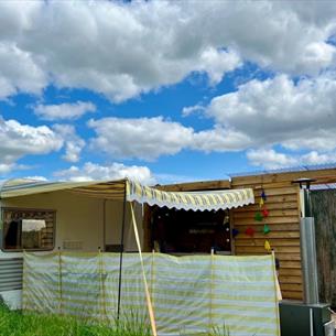 Outside view of vintage caravan with yellow awning, decking area and toilet/shower building