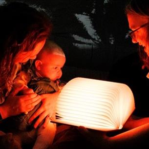 Two adults and a baby looking at an illuminated open book