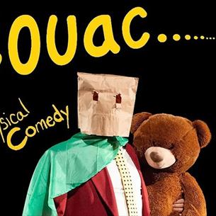 person wearing a suit with a green cape, a brown paper bag on head, holding a teddy bear