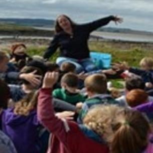 Storyteller, Elizabeth Baker, entertaining a group of children with her arms outstretched.