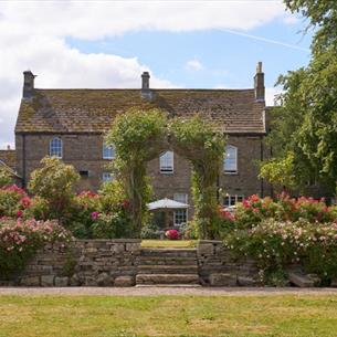View of the main house at Lord Crewe Arms surrounded by flowers in the garden on a bright sunny day.
