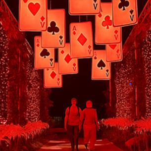 Adventures in Wonderland. Two people walking through a red tunnel of lights, beneath suspended playing cards.