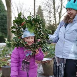 A child and an adult in the grounds of Ushaw peering through a handmade festive wreath.