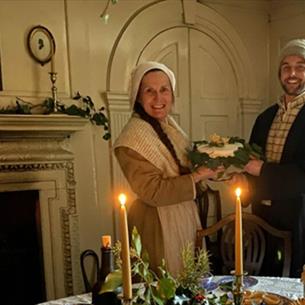 Two members of staff in Georgian clothing, holding Christmas cake.