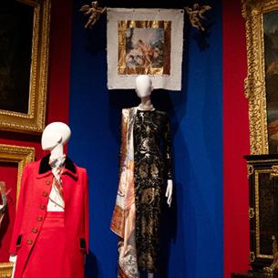 Photograph of a museum display featuring historical and artistic elements, including two mannequins dressed in elaborate costumes and framed classical