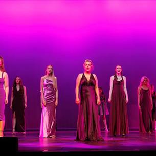 Performing Arts students of New College Durham's Class of 2025 on stage in long dresses.