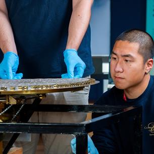 Two individuals examining a large, circular mechanical device with intricate components, possibly an antique or scientific instrument.