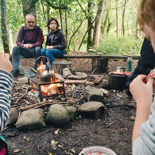 Children, accompanied by adults, enjoying bread on a stick by the campfire.