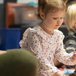 Child holding a crayon, sitting with other children at Little Dragons.