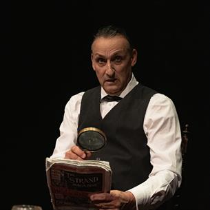Sherlock Holmes reading a newspaper through a magnifying glass