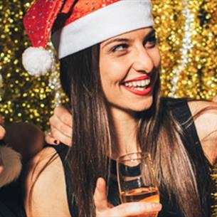 3 women in Santa hats laughing and drinking from champagne flutes.