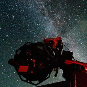 A telescope silhouetted against a Star-filled night sky, with the Milky Way visible in the background.