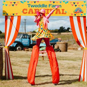 A performer singing on stilts between rolls of hay at Tweddle Carnival.