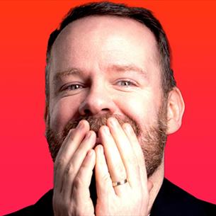 Headshot of Neil Delamere grinning with his hands covering his mouth.