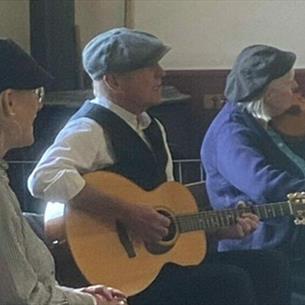 Folk musicians playing together in the Band Hall in The Pit Village.