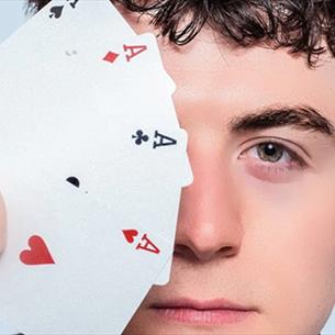 Close up of Tom Bolton holding a suit of aces which cover one side of his face. 