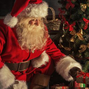 Santa placing presents under a tree.