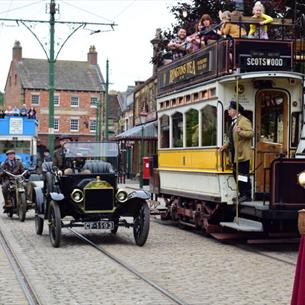 Staff in character at Beamish Museum, next to vintage cars and a tram - 1900s Town