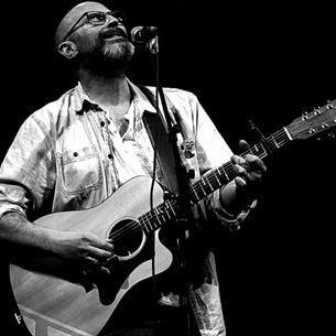 Black and white image of Steve Pledger playing guitar and singing on stage 