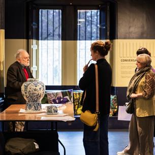 Photograph of a museum or gallery setting where a guide explains exhibits to a group of four visitors. 