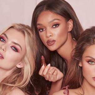 Three people holding Charlotte Tilbury makeup against a light pink background
