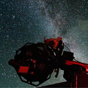 A telescope silhouetted against a star-filled night sky, with the Milky Way visible in the background.