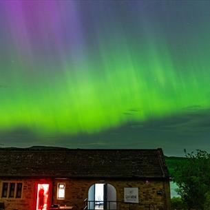 Brightly coloured aurora visible in the dark night sky above Grassholme Observatory and Reservoir
