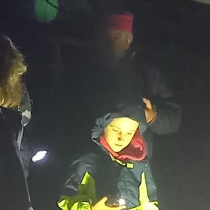 Participants in warm clothing gather around a moth trap during a nighttime wildlife survey, illuminated by a bright light.