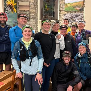 Group of runners wearing head torches pose together indoors after a night time run.
