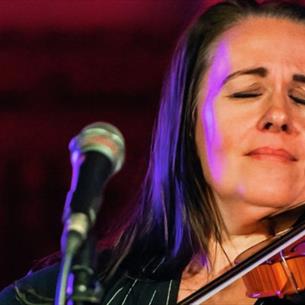 A close up image of a person playing the violin with their eyes closed on a stage.