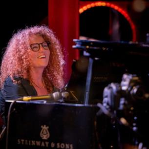 Person smiling whilst playing the piano on stage.