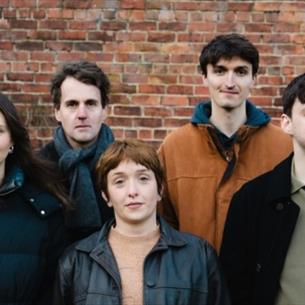 Seven people stood against a brick wall.