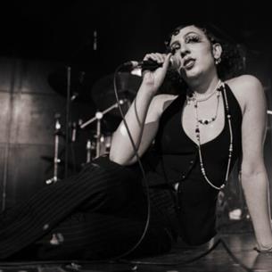 A person sat on stage singing into a microphone, the image is in black and white.