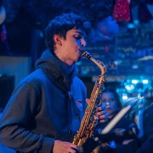 A person playing the saxophone, with a blue background. 