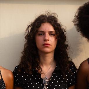 Three people standing against a wall, looking straight ahead at the camera.