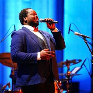 A person singing into a microphone on a blue stage.