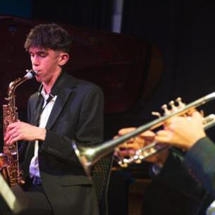 Two people sat down on stage playing brass instruments.