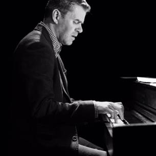 The side profile of a person playing the piano, the image is in black and white.