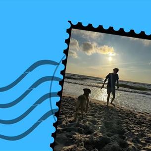 Letter stamp with an image of a silhouetted figure with a dog on the beach at sunset. Blue background.