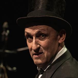 Man wearing a top hat and suit, looking over his shoulder with a shocked expression, shrouded in darkness.